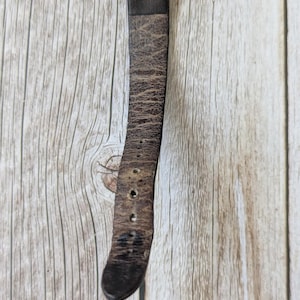 Pu&ograve; includere: Primo piano di un orologio da polso con quadrante argentato e cinturino in pelle marrone usurata. Il cinturino mostra segni di usura, con pieghe e fori di regolazione. L'orologio &egrave; posto su uno sfondo di legno chiaro.