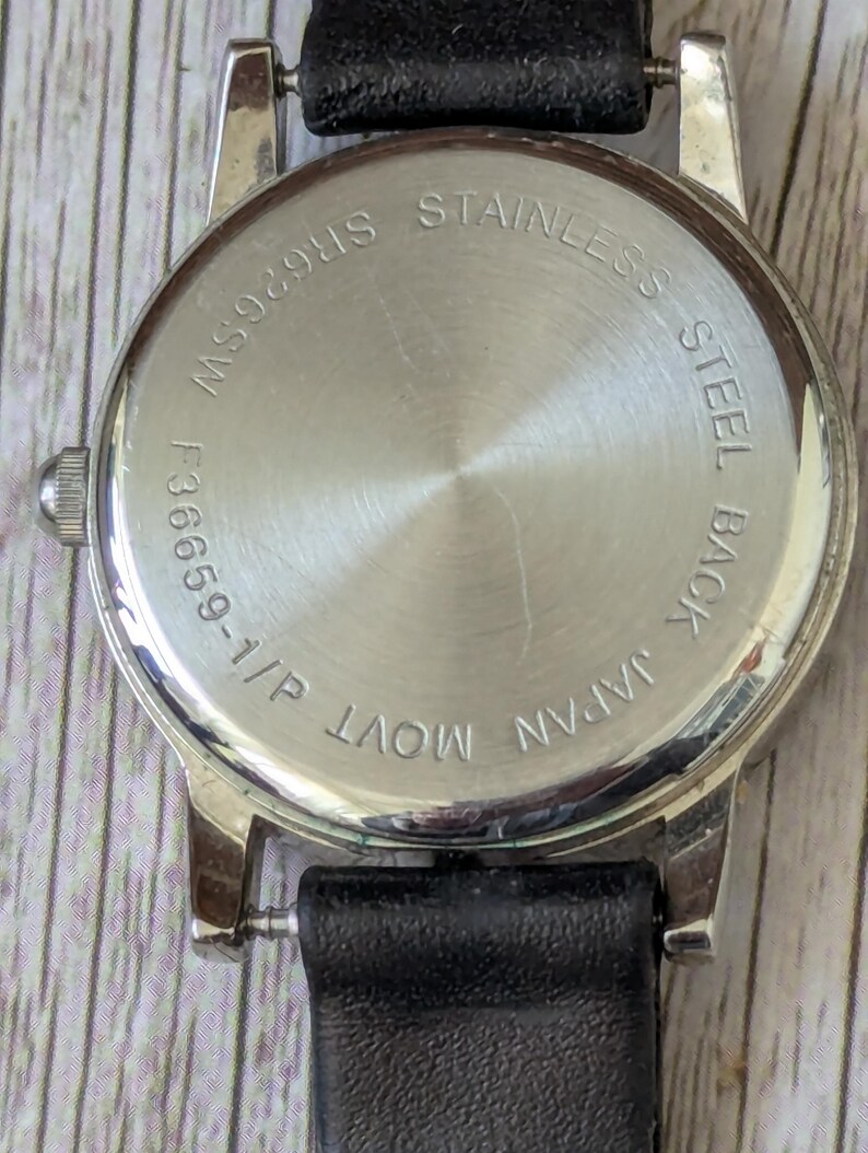 Pu&ograve; includere: Primo piano del retro di un orologio da polso con cinturino in pelle nera. Il retro dell'orologio &egrave; argentato con le scritte "STAINLESS STEEL BACK" e "JAPAN MOVT" incise. La cassa dell'orologio &egrave; argentata.