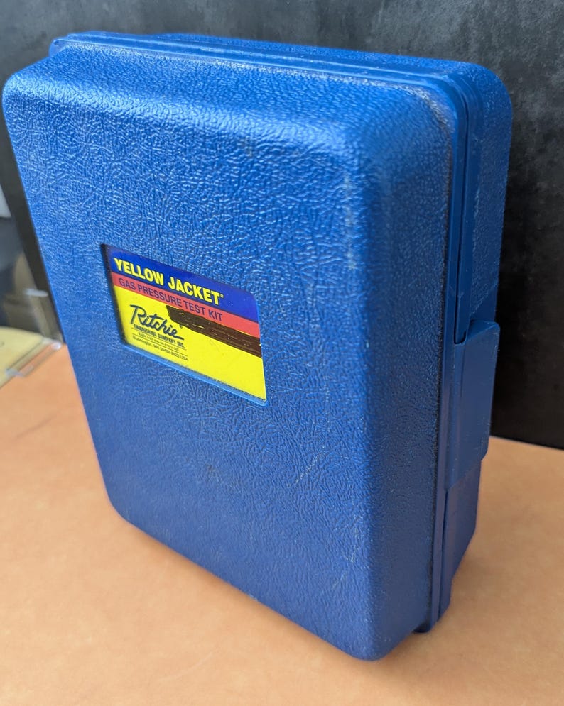May include: A blue plastic case with a textured surface. The case has a rectangular label that reads "YELLOW JACKET GAS PRESSURE TEST KIT" and the Ritchie logo. The case is closed and appears to be a tool case.