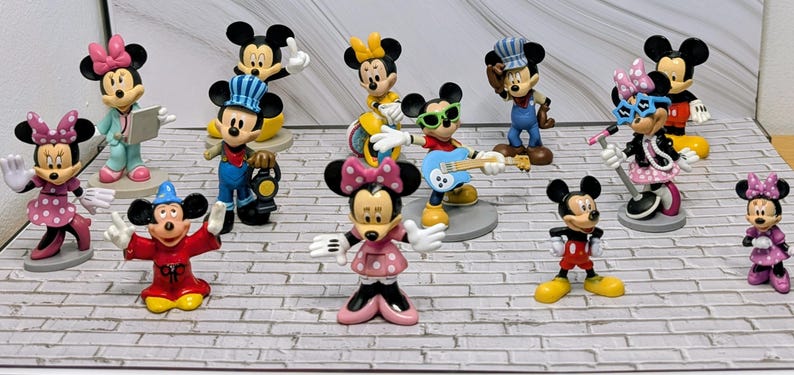 May include: A collection of Mickey and Minnie Mouse figurines in various poses and outfits. The figurines are brightly colored and include Mickey as a conductor, a magician, and a guitarist. Minnie is shown in several outfits, including a pink polka-dot dress.