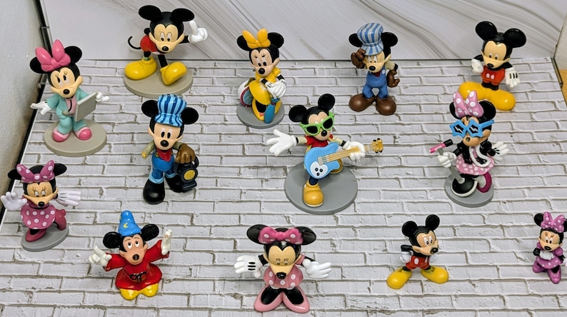 May include: A collection of colorful Mickey Mouse and Minnie Mouse figurines in various poses and outfits. Some figures are dressed as a conductor, a guitarist, and a magician. The figurines are on individual circular bases.
