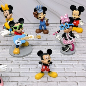 May include: A collection of Mickey and Minnie Mouse figurines in various poses. Mickey is depicted playing a blue guitar, wearing sunglasses, and dressed in a red shirt. Minnie is shown with a microphone, wearing a pink polka dot dress and star-shaped glasses.