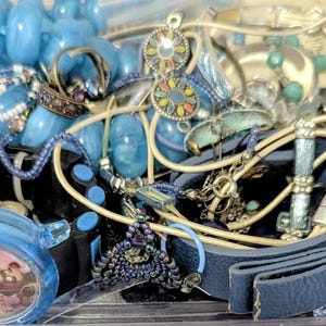 May include: A collection of assorted jewelry and accessories including a blue beaded necklace, a blue leather-like bracelet with a gold-tone metal accent, a black digital watch with a character face, and various metal charms and beaded strands.