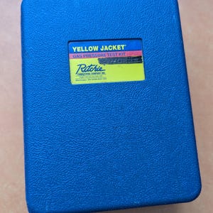 May include: A blue, rectangular case with a textured surface. The case has a yellow label with the text "YELLOW JACKET GAS PRESSURE TEST KIT" and the Ritchie Engineering Company Inc. logo.