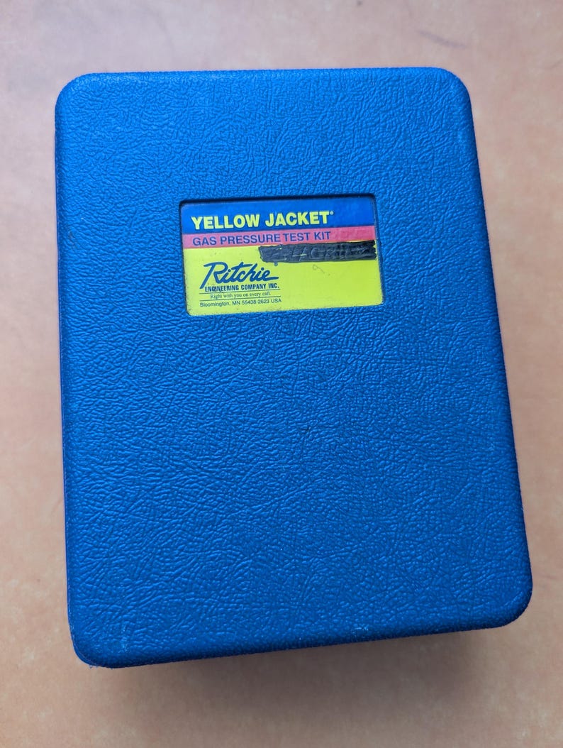 May include: A blue, rectangular case with a textured surface. The case has a yellow label with the text "YELLOW JACKET GAS PRESSURE TEST KIT" and the Ritchie Engineering Company Inc. logo.