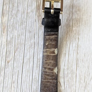 Pu&ograve; includere: Primo piano di un cinturino per orologio con fibbia color oro. La fibbia &egrave; incisa con la parola "Speidel". Il cinturino &egrave; in pelle nera con segni di usura.