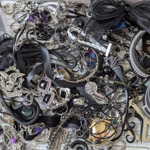 May include: A large collection of assorted jewellery including black ribbon chokers, silver-tone chains, bracelets with rhinestones, a metal eagle emblem with 1776-1976 text, a peace sign pendant, and a packaged industrial piercing accessory.