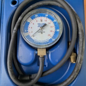May include: A blue and white pressure gauge with a black hose coiled around it. The gauge reads "YELLOW JACK" and "LOW PRESSURE" with measurements in ounces per square inch. The gauge is housed in a blue plastic case.