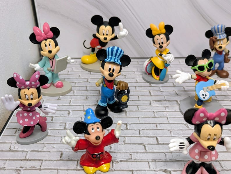 May include: A collection of Mickey Mouse and Minnie Mouse figurines in various outfits and poses. The figurines include Mickey as a conductor, a magician, and a guitarist. Minnie is depicted as a doctor and in a polka dot dress. The figurines are on gray circular bases.