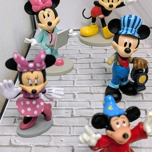 May include: A collection of Mickey Mouse and Minnie Mouse figurines in various poses. Minnie is shown in a pink polka dot dress and a pink bow. Mickey is depicted in several outfits, including a conductor, a magician, and a classic pose.