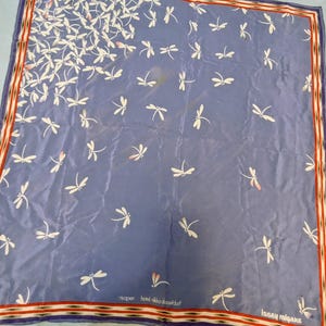 May include: A square blue scarf featuring a repeating pattern of white dragonflies with subtle pink accents. The border consists of thin red, white, and black stripes. The text '78 open hotel nikko dusseldorf' and 'issey miyake' are printed.