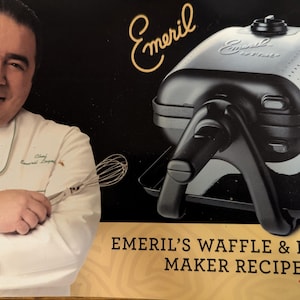 Peut inclure: Image d'un gaufrier et appareil à panini Emeril. Le gaufrier est noir et argenté avec le logo Emeril. L'image présente également un chef tenant un fouet et le texte "Emeril's Waffle & Panini Maker Recipes."