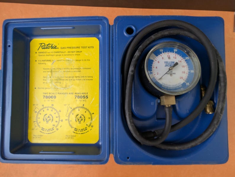 May include: A blue Ritchie gas pressure test kit with a yellow insert. The kit includes a pressure gauge with a black hose and the text "YELLOW JACKET". The kit is open, revealing instructions and two scale ranges.