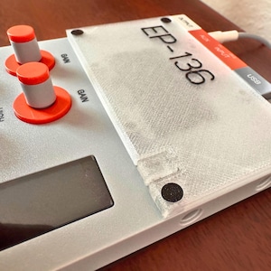 May include: A light gray electronic device with orange and gray knobs and the text "EP-136". The device has a clear plastic cover and a USB port. A gray cable is connected to the device.