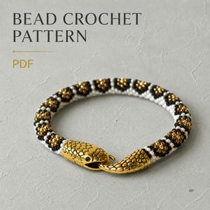 Könnte beinhalten: Ein Perlenhäkelarmband mit einem sich wiederholenden geometrischen Muster aus weißen, schwarzen und goldfarbenen Metallperlen. Das Armband hat einen goldfarbenen Metallverschluss in Schlangenkopfform. Der Text BEAD CROCHET PATTERN PDF ist sichtbar.