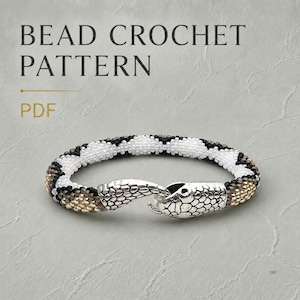 Pode incluir: Um padrão de crochê com miçangas em PDF apresentando uma pulseira com um padrão geométrico repetitivo em miçangas brancas, pretas e douradas metálicas. A pulseira termina em um fecho de metal prateado em forma de cabeça de cobra.