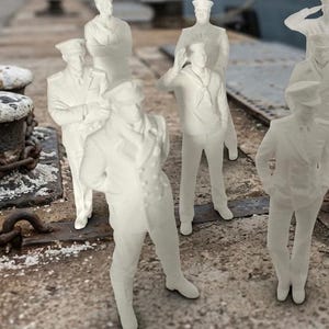 Könnte beinhalten: Eine Ansammlung kleiner, cremefarbener Figuren von Marineuniformierten, die auf einem verwitterten Betonpier stehen. Im Hintergrund ein großes Schiff, im Vordergrund Poller und Ketten. Die Figuren befinden sich in verschiedenen Posen.