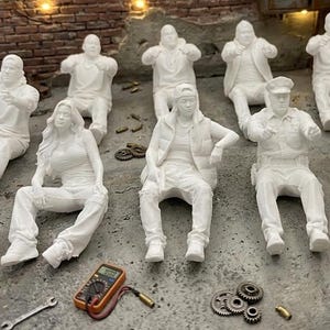 Könnte beinhalten: Eine Diorama-Szene mit kleinen weißen Figuren von Menschen in verschiedenen Posen, darunter sitzende Positionen. Der Hintergrund umfasst eine Backsteinmauer, einen Metallschrank und eine Uhr. Verschiedene Werkzeuge und Zubehör sind um die Figuren herum verstreut.