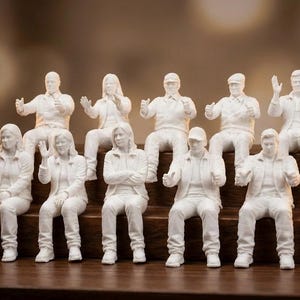 Peut inclure: Onze figurines blanches représentant des personnes dans diverses poses assises et debout. Les figurines sont disposées sur une surface en bois à plusieurs niveaux. Certaines personnes saluent ou font un signe de pouce.