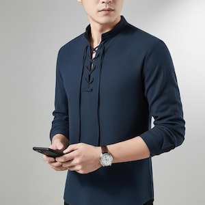May include: Navy blue long-sleeve shirt with a mandarin collar and a lace-up neckline. The shirt has a relaxed fit and is made of a soft, breathable fabric. The sleeves have buttoned cuffs. A classic and versatile piece for any wardrobe.