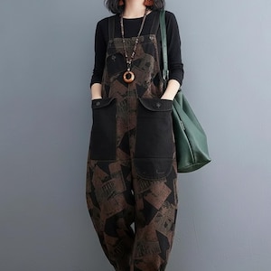 Puede incluir: Mono con top negro y bolso verde. El mono tiene un estampado geométrico marrón y negro en las piernas y el pecho. El pecho y los bolsillos son de color negro liso. La modelo lleva un collar largo y pendientes.