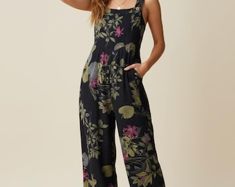 May include: Black jumpsuit with a floral pattern featuring green, pink, and gray leaves and flowers. The jumpsuit has a square neckline, wide legs, and button details on the straps. It includes pockets.