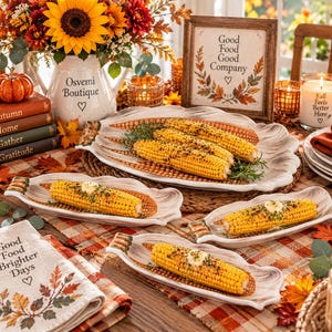 May include: A collection of ceramic corn-shaped serving dishes featuring a cream-colored finish with brown accents. The dishes hold cooked corn on the cob topped with butter and herbs. The set includes one large oval platter and three smaller individual dishes.