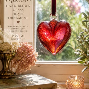 May include: A red hand-blown glass heart ornament suspended by a dark red velvet ribbon. The glass features a textured, speckled appearance. Text on the image reads: SECOND BLOOM VINTAGE MEXICAN HAND-BLOWN GLASS HEART ORNAMENT HANDMADE BEAUTY. TIMELESS JOY. A SECOND BLOOM. OSVEMI BOUTIQUE.