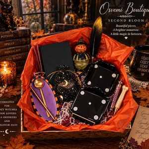 May include: A gift box filled with orange tissue paper containing a black notebook, a pumpkin figurine, a black drawstring pouch with gold moon and star prints, two black dice-shaped containers, a purple oval tray, gold spoons, and pens.