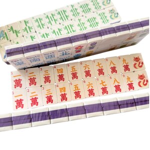 May include: A set of white mahjong tiles arranged in rows. The tiles feature green bamboo patterns, red and orange Chinese characters, directional labels like East, South, West, and North, and colorful illustrations of flowers, birds, and dragons.