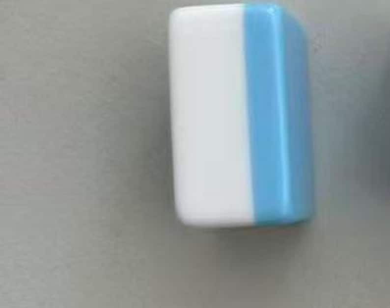 May include: A rectangular block with rounded corners, featuring a smooth, glossy finish. The object is divided vertically into two distinct colour sections, with a solid white panel on the left side and a solid light blue panel on the right side.