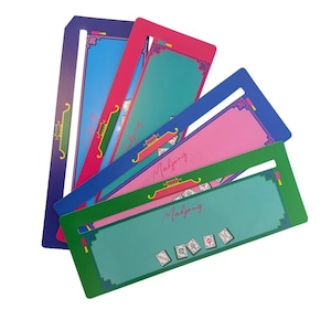 Puede incluir: Una colección de coloridos tableros de juego de Mahjong en tonos de azul, rosa, verde y morado. Cada tablero presenta un borde decorativo y la palabra "Mahjong" en cursiva. Algunos tableros muestran fichas de Mahjong.