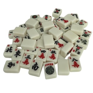 May include: A collection of off-white Mahjong tiles with black and red symbols and characters. Some tiles feature floral designs, numbers, and the word "JOKER". The tiles are scattered, suggesting a game in progress.