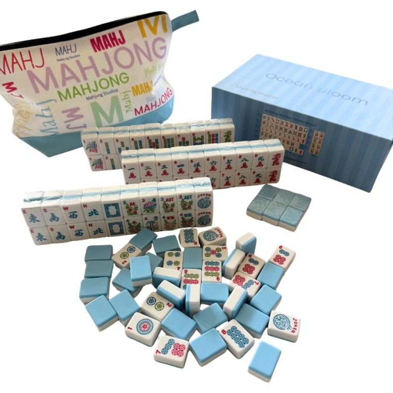 May include: A Mahjong game set featuring white and light blue tiles with colourful character, bamboo, and dot markings. The set includes a light blue storage box labelled Ocean Bloom, a zippered pouch with the text Mahjong, and numerous loose tiles.