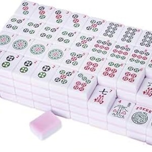 May include: A complete Mahjong set with white tiles featuring red, green, and black symbols and numbers. The set includes two pink dice. The tiles are stacked and arranged, ready for play.