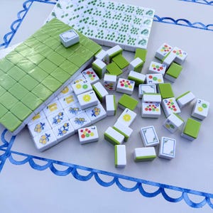 May include: A set of white mahjong tiles with lime green backs, featuring colorful illustrations of citrus fruits like lemons, limes, and oranges, along with numerical markings and decorative floral borders on some tiles, arranged in stacks and scattered.