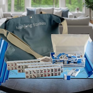 May include: A complete Mahjong set with blue and white tiles, a blue tote bag with "Mahjong Studios" printed on it, and a clear plastic container. The set includes racks, dice, and a blue playing surface.