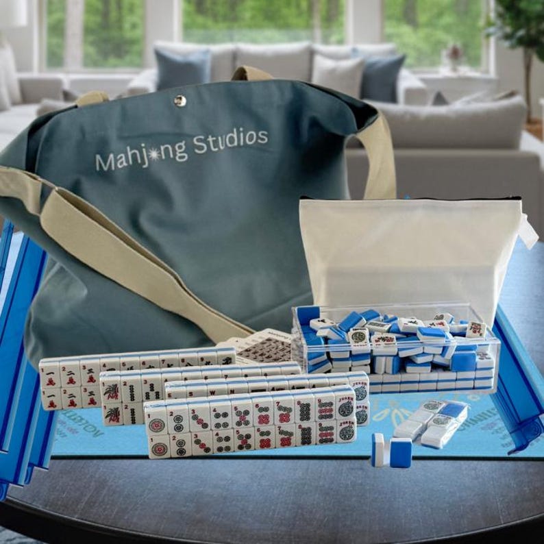 May include: A complete Mahjong set with blue and white tiles, a blue tote bag with "Mahjong Studios" printed on it, and a clear plastic container. The set includes racks, dice, and a blue playing surface.