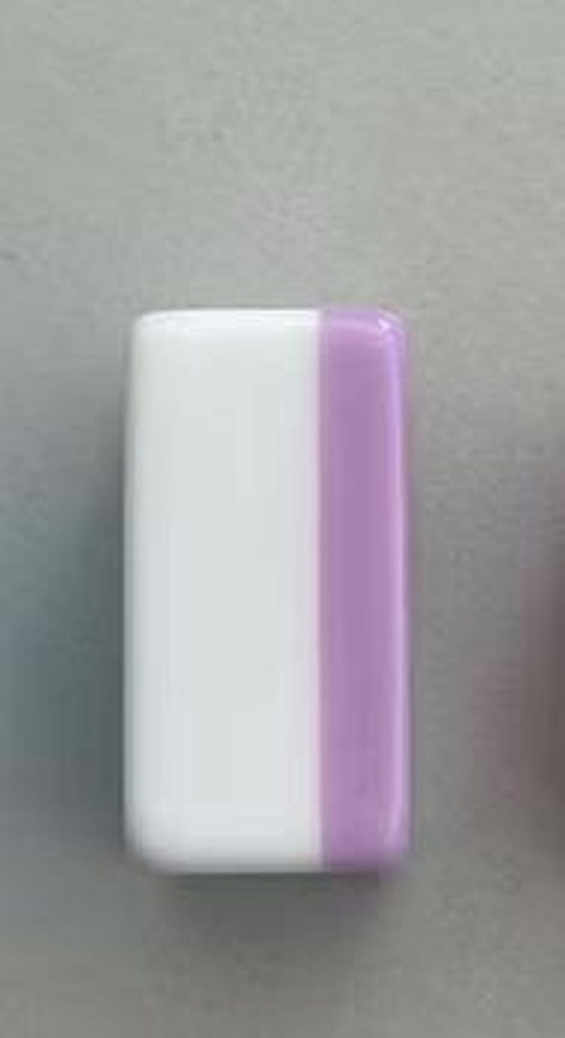 May include: A rectangular block with rounded corners featuring a smooth, glossy finish. The object is divided vertically into two distinct sections, with a larger white portion on the left and a smaller, solid light purple section on the right side.
