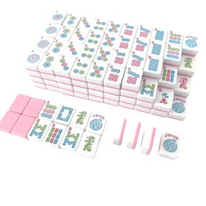 May include: A complete Mahjong set with white tiles featuring pink edges and colorful symbols. The set includes tiles with numbers, characters, and Jokers, arranged in stacks and rows. The game pieces are displayed on a white surface.
