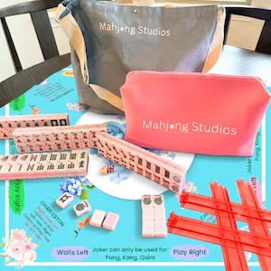 May include: A complete Mahjong set with pink tiles, dice, and a red rack, displayed on a blue floral patterned surface. Includes a gray tote bag and a pink zippered pouch, both with "Mahjong Studios" printed on them.