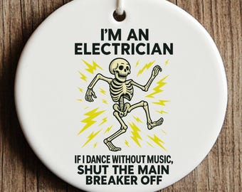 May include: A round white ceramic ornament featuring a black graphic of a skeleton dancing amidst yellow lightning bolts. The text reads: I'M AN ELECTRICIAN IF I DANCE WITHOUT MUSIC, SHUT THE MAIN BREAKER OFF. A white string is attached for hanging.