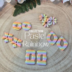 Peut inclure: Une collection de boucles d'oreilles pastel arc-en-ciel de différentes formes, dont des donuts, des fleurs et des gouttes. Les boucles d'oreilles sont disposées sur une surface en bois, avec le texte "Collection Pastel Rainbow".