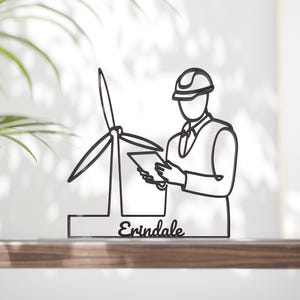 Könnte beinhalten: Schwarze Metallskulptur, die einen Ingenieur mit einer Windkraftanlage und einem Tablet darstellt. Das Wort "Erindale" ist an der Basis geschrieben. Die Skulptur ist im Strichstil gehalten und steht auf einer Holzoberfläche.