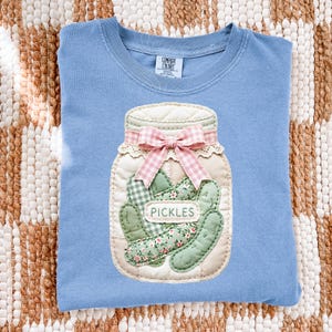A blue t-shirt with a hand-sewn patch depicting a jar of pickles.