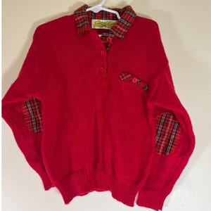 May include: A red sweater with a plaid collar, elbow patches, and pocket detail. The sweater has a button-down neckline and a ribbed hem. The brand name "Star-S" is visible on the collar.