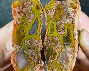May include: Two halves of a cut agate stone, showcasing a vibrant display of colors. The stone features layers of yellow, orange, and brown hues, with intricate patterns and a polished surface. The agate's natural beauty is highlighted in this close-up view.