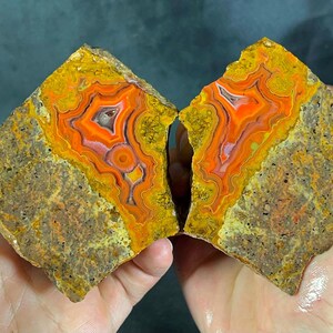 Puede incluir: Dos mitades de una roca partida que presentan bandas concéntricas vibrantes de ágata naranja, roja y blanca, rodeadas por una corteza exterior rugosa, texturizada y de color marrón amarillento. El interior muestra patrones minerales ondulados.