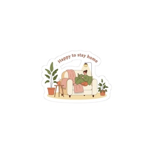 May include: A sticker featuring a cozy scene of a person reading on a cream-colored couch with a pink blanket and a cat. The text "Happy to stay home" arches above the scene, with potted plants and a small table with a mug.