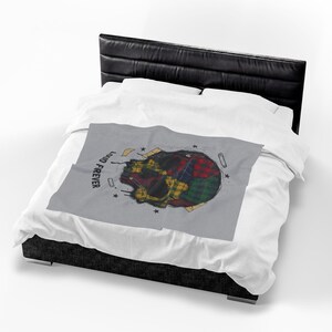 Pode incluir: Um cobertor cinza com um desenho de caveira. A caveira é composta por um patchwork de padrões xadrez em vermelho, verde, amarelo e azul. As palavras "LOUD FOREVER" são impressas no cobertor.
